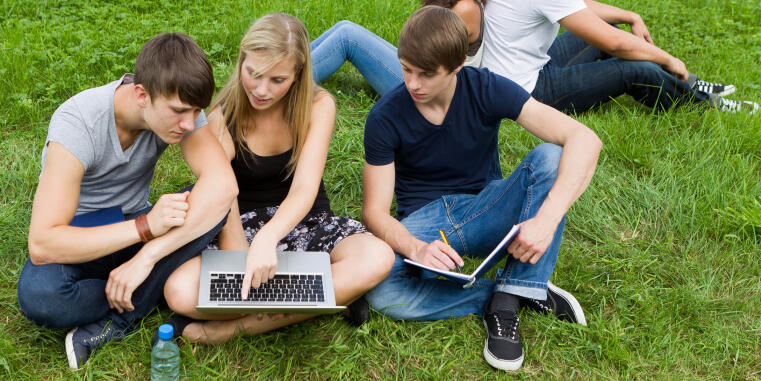 Drei Studierende sitzen mit einem Laptop auf dem Rasen