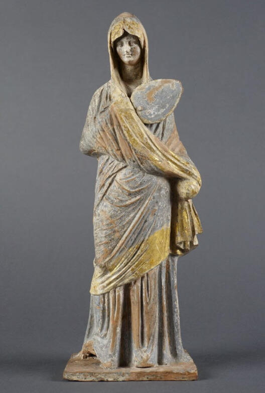 Das Bild zeigt die Tanagräerin mit dem Namen „Dame en bleu“. Sie wurde in Tanagra gefunden und zwischen 325 bis 300 v. Chr. datiert. Heute befindet sie sich in Paris.