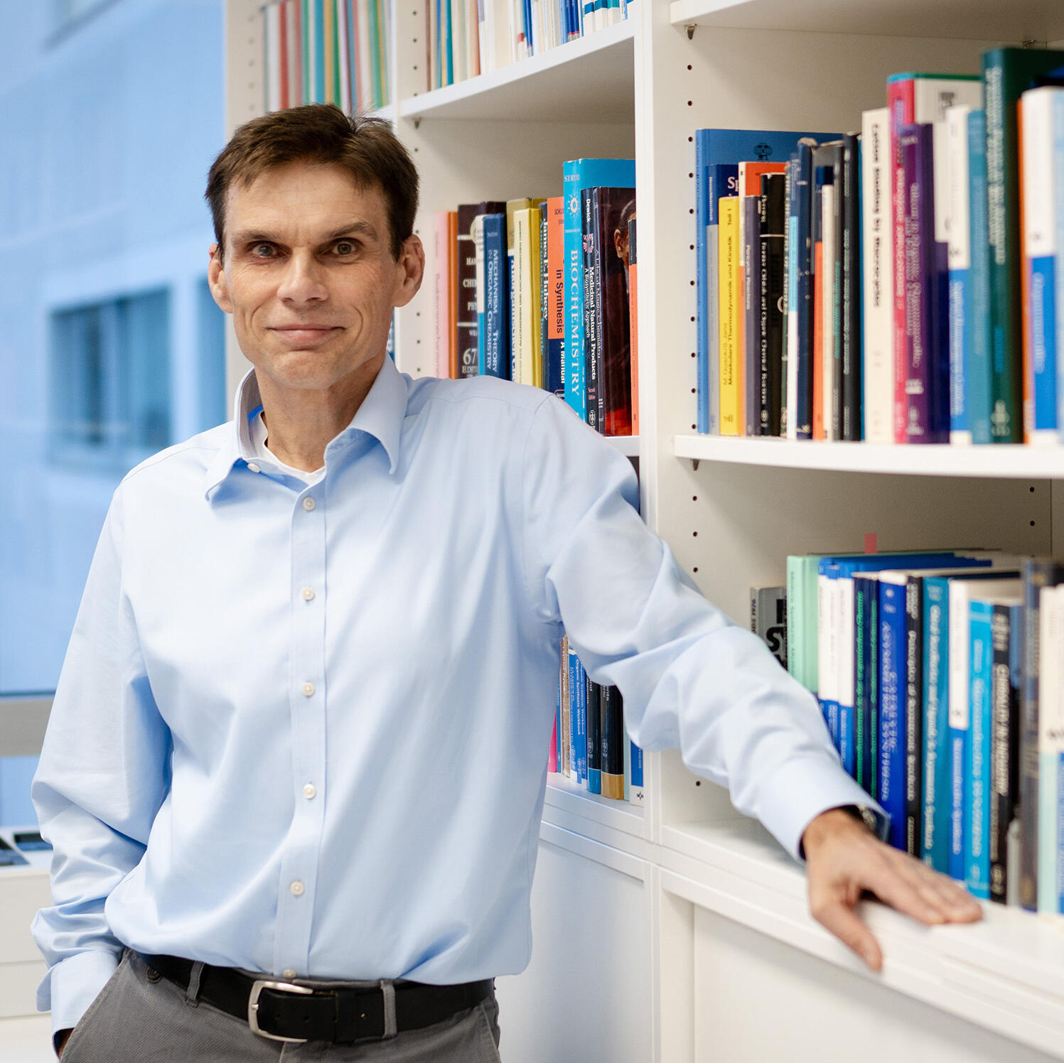 Professor Armido Studer lehnt an einem Bücherregal mit chemischen Fachbüchern.