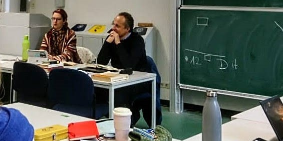 Magistra Eva Pauschatz und Professor Grünstäudl sitzen an einem Pult und unterrichten gemeinsam. 