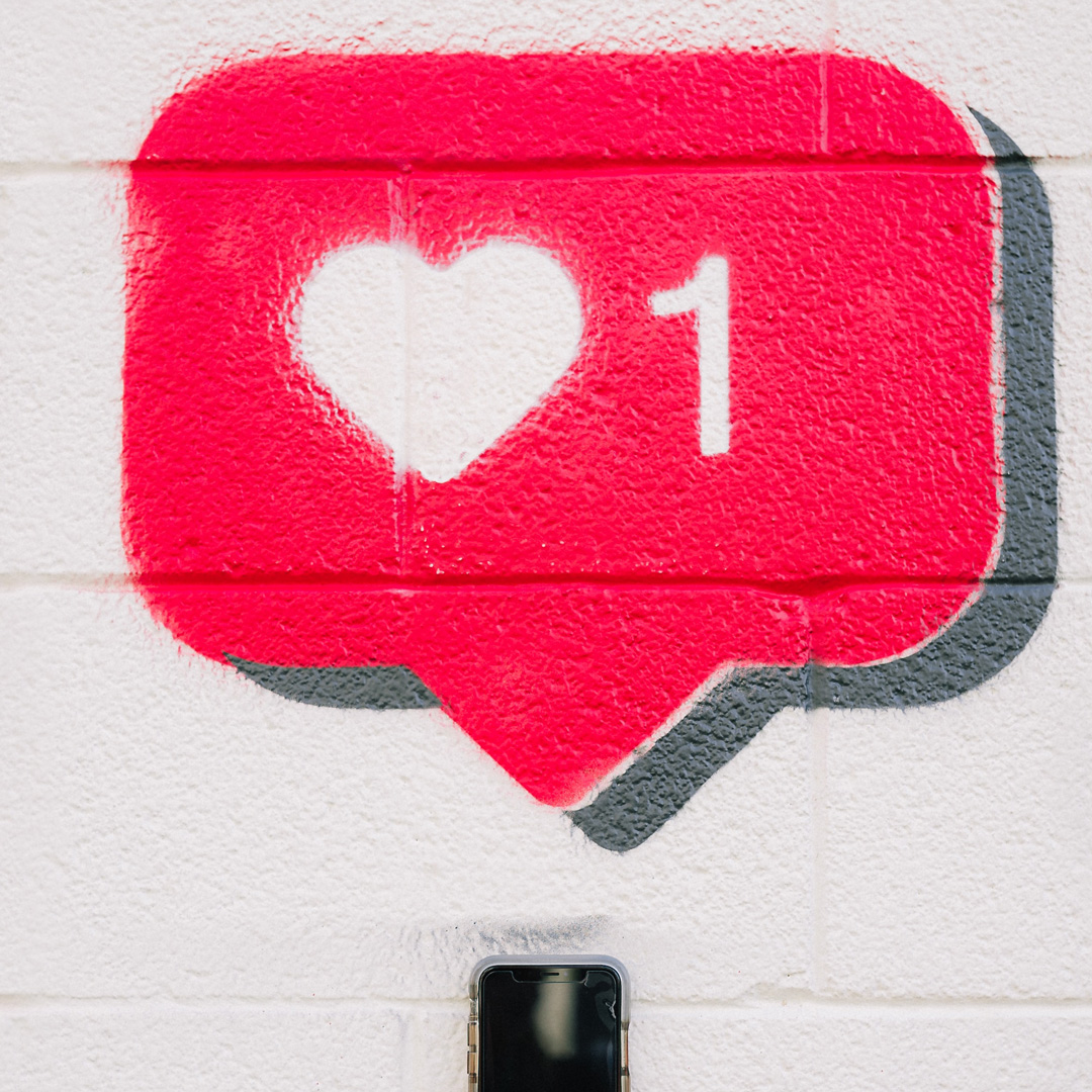 Ein Graffitti einer Sprechblase mit einem Herz und der Zahl Eins darin. Unten am Bildrand ein Smartphone.