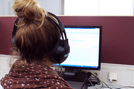 Eine Studentin blickt auf einen Bildschirm, sie trägt Kopfhörer. 