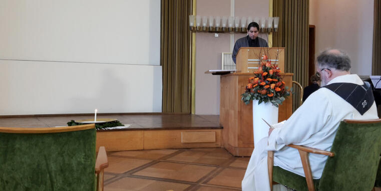 Prof. Dr. Mouhanad Khorchide hinter einem Rednerpult, im Vordergrund sitzt ein Priester mit dem Rücken zum Betrachter
