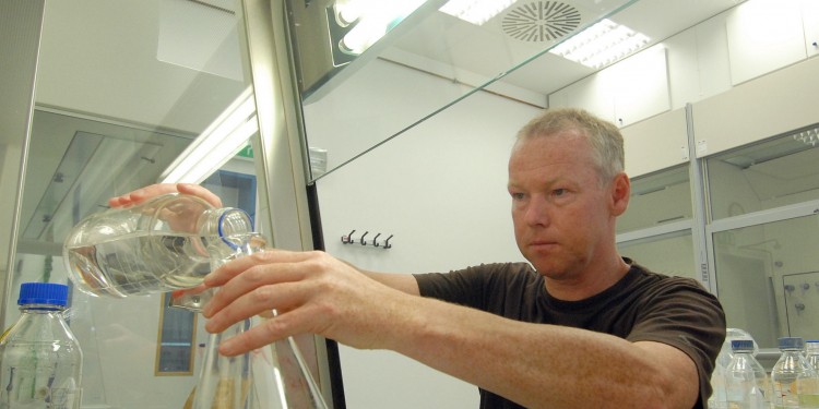 Prof. Dr. Michael Hippler mit seinen Forschungsobjekten - grünen einzelligen Algen - im Glaskolben.<address>© WWU - Grewer</address>