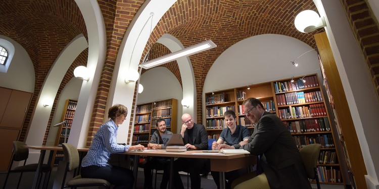 Prof. Lutz Doering (r.) und die Studierenden lesen und lernen gerne in der Bibliothek im ehemaligen Kapellenraum.<address>© WWU / Peter Grewer</address>