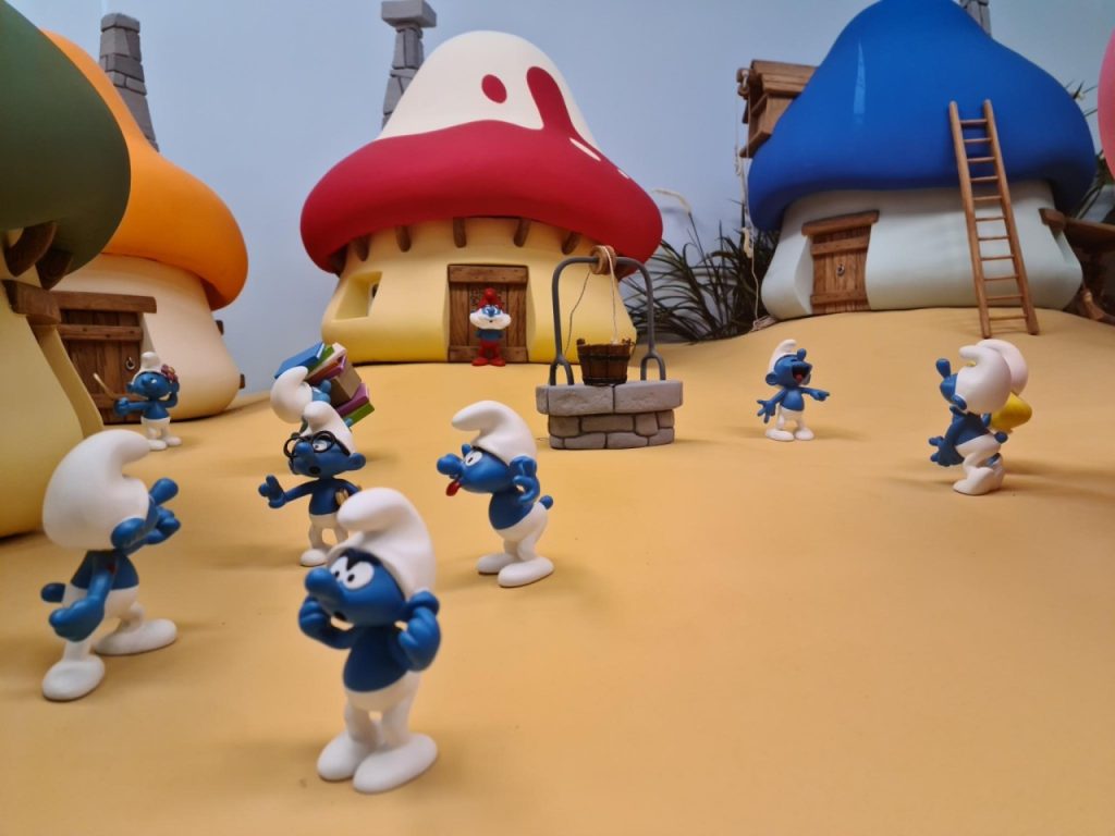 kleine blaue Schlümpfe stehen vor ihren pilzförmigen, bunten Häusern.