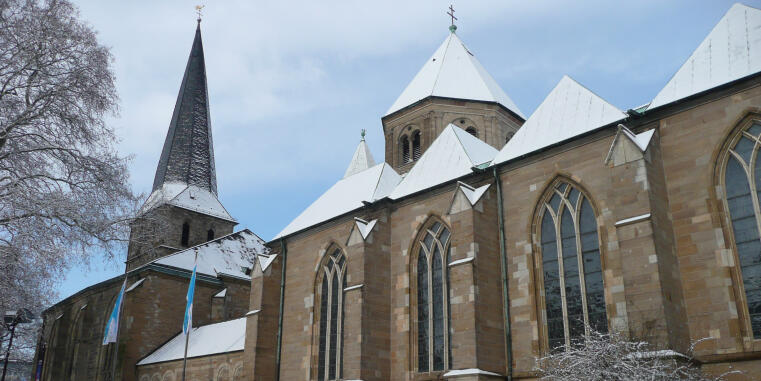 Large Gothic church with a tall dark spire, snow-covered roofs, and long pointed-arch windows.