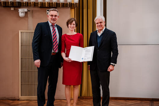 Eine Frau hält ein Dokument. Rechts und links von ihr steht jeweils ein Mann.