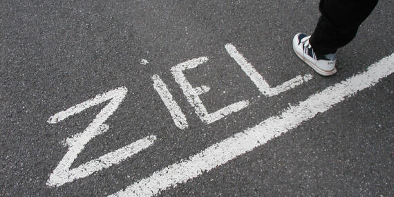 Finish line on a street drawn with chalk, above the word "ZIEL" is written on the ground. A foot crosses this line.
