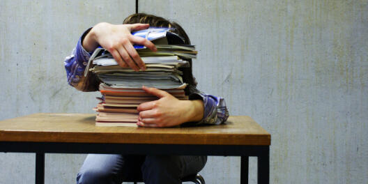 large pile of notebooks on a table hiding the person behind them