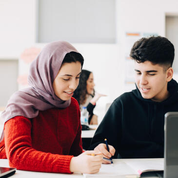 Male and female students discussing together while studying in classroom
