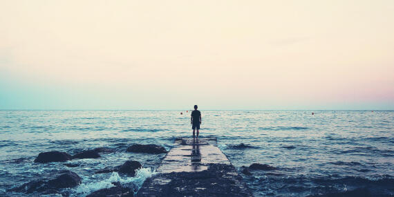 Person, die am Meer steht und auf den Horizont blickt