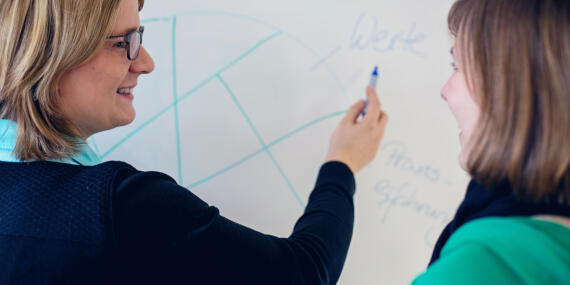 Frau mit einem Stift in der rechten Hand vor einem Whiteboard