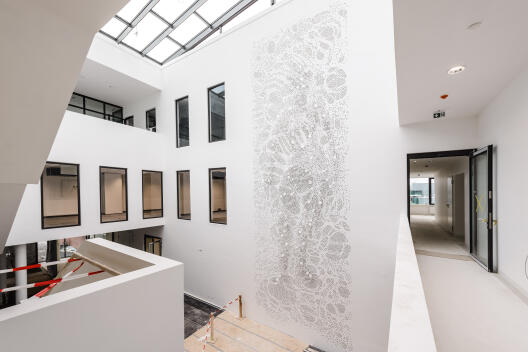 A twelve-meter-high artwork entitled “Auf|Lösung” (Re|Solution) was installed in the foyer of the Multiscale Imaging Centre in spring 2021. In this newly emerging research building at the University of Münster, scientists will investigate how cells behave in organisms – to this end, they employ and develop innovative imaging methods. The wall installation imitates the process of visually resolving the human organism into its building blocks using different sized dots as abstract symbols for cells and molecules.
