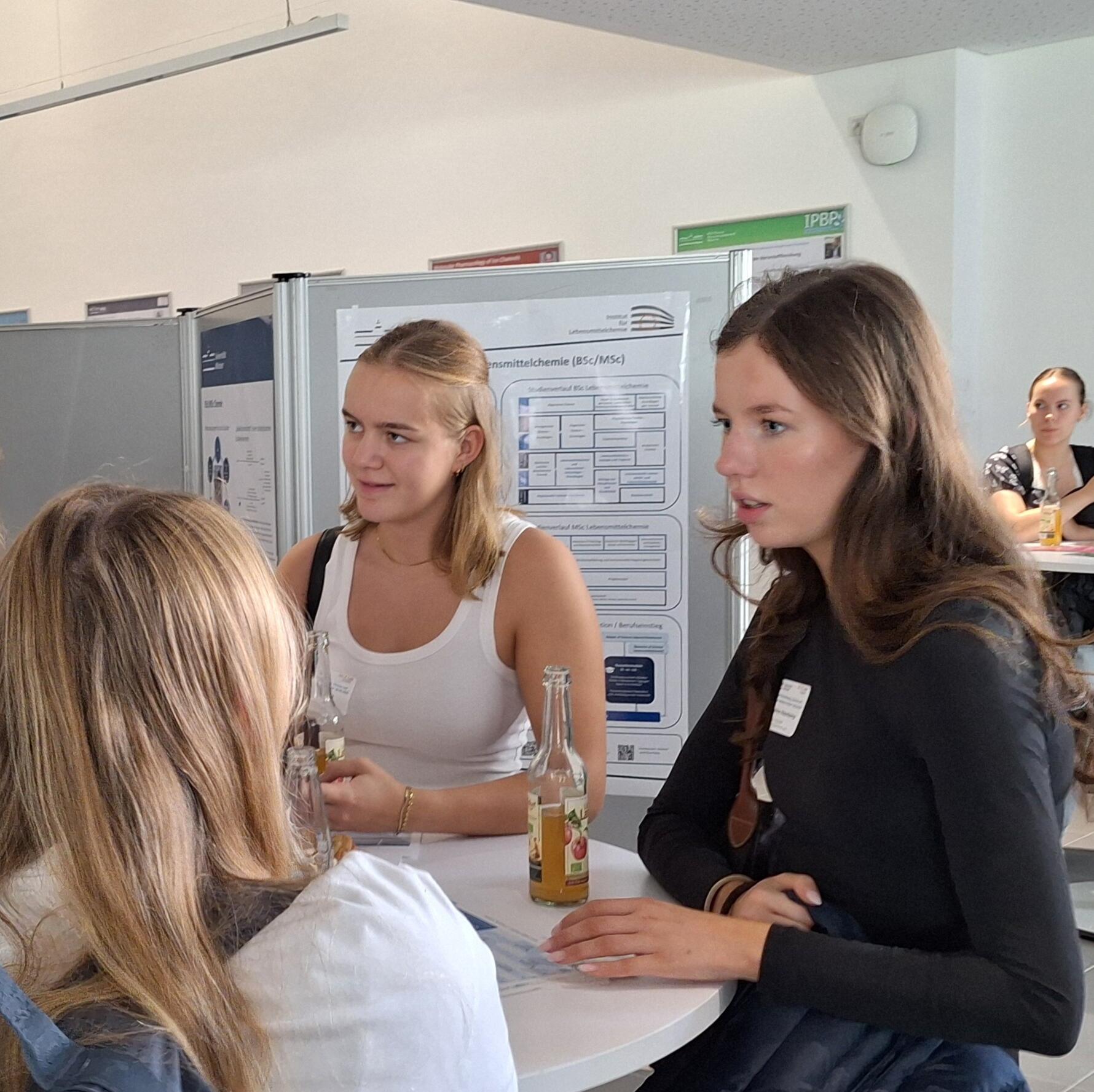 Schülerinnen diskutieren an einem Stehtisch vor einem Übersichtsposter.