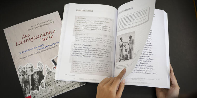 Man sieht das aufgeschlagene Arbeitsbuch, daneben eine geschlossene Version mit dem Cover. 
