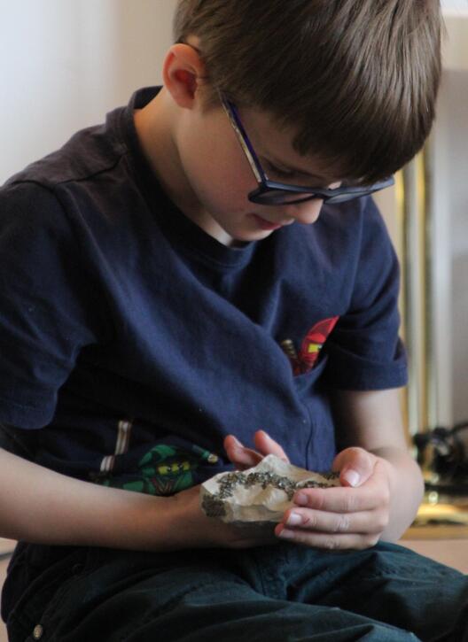 Ein Kind betrachtet ein Gestein, durch das sich eine Mineralader zieht.