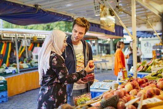 Frau mit Kopftuch und Mann stehen am Obststand auf dem Markt