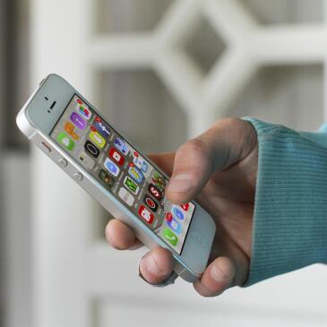 Smartphone in einer Hand, auf dem Display sind Apps zu erkennen