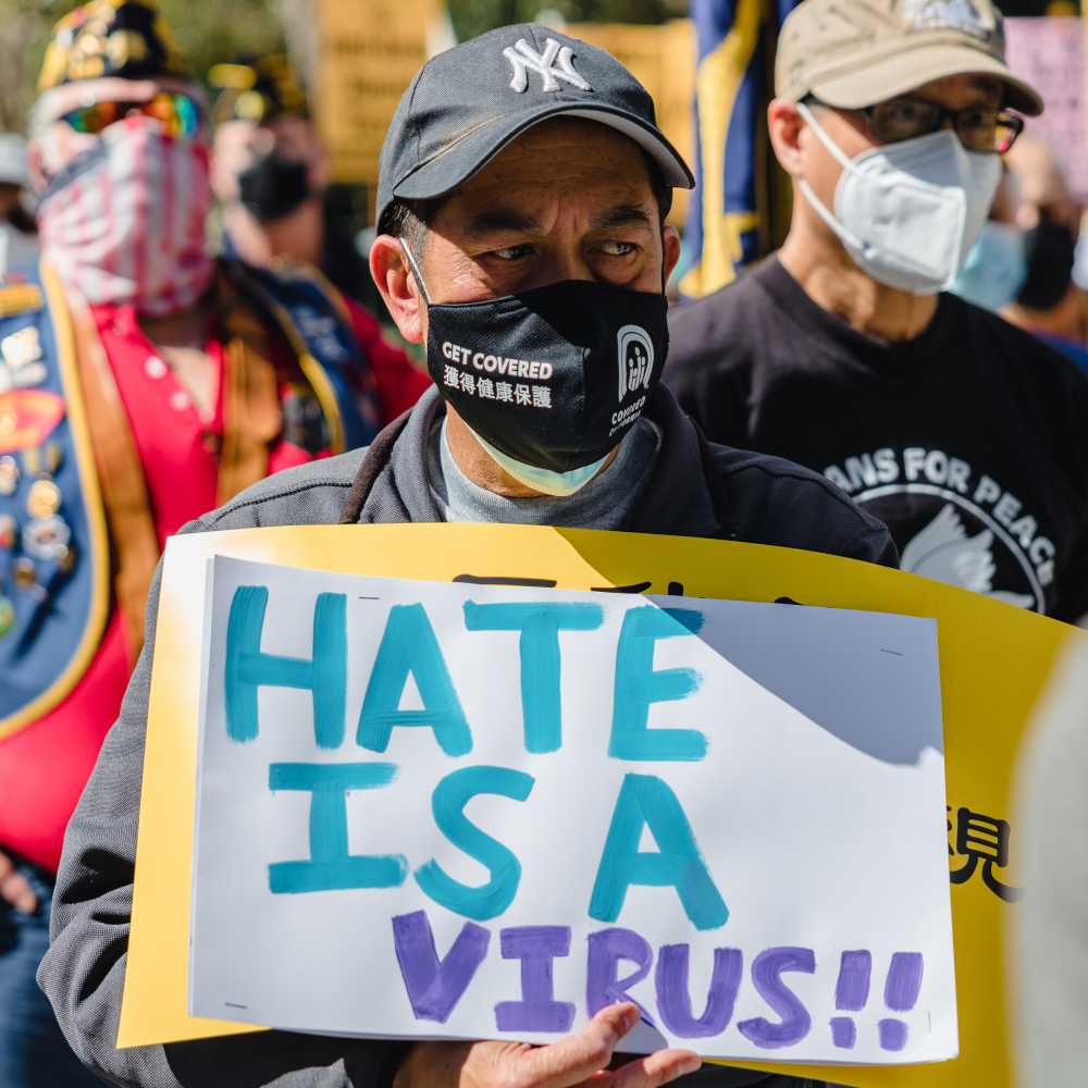 Ein Protestierender trägt ein Schild mit der Aufschrift "Hate Is A Virus"