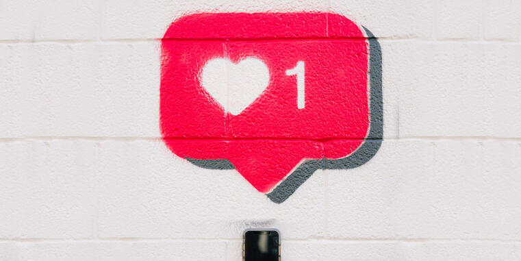 Ein Graffitti einer Sprechblase mit einem Herz und der Zahl Eins darin. Unten am Bildrand ein Smartphone.