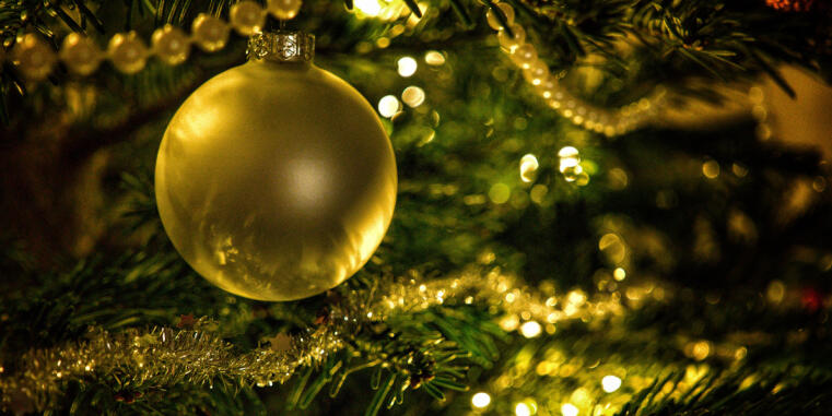 Nahaufnahme eines geschmückten Weihnachtsbaumes mit vielen goldenen Ketten. Im Fokus ist eine goldene Weihnachtskugel.