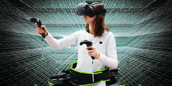 Eine Studentin trägt eine VR-Brille sowie Hand-Controller. Sie steht dabei in einer grünen, abstrakten Umgebung.