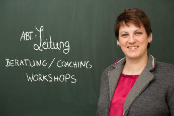 Foto von Doktor Claudia Bendick vor einer Tafel mit den Worten Leitung, Beratung, Coaching, Workshops