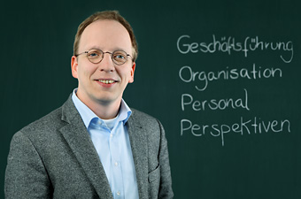 Foto von Doktor Martin Jungwirth vor einer Tafel mit den Worten Geschäftsführung, Organisation, Personal, Perspektiven