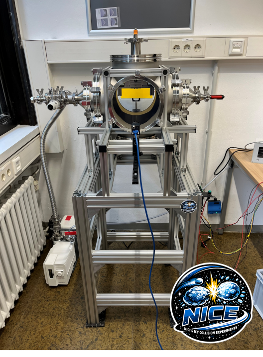 Setup des NICE Experiments. Zu sehen ist eine Vakuumkammer mit großem Sichtfenster auf einem stabilen Grundgerüst.