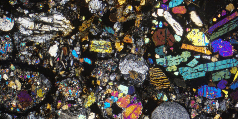Ein Ausschnitt eines Dünnschliffs des Meteoriten Dhajala. Zu sehen sind runde Partikel, sogenannte Chondren, und verschiedenfarbige Minerale, die in einer feinkörnigen Grundmasse liegen.