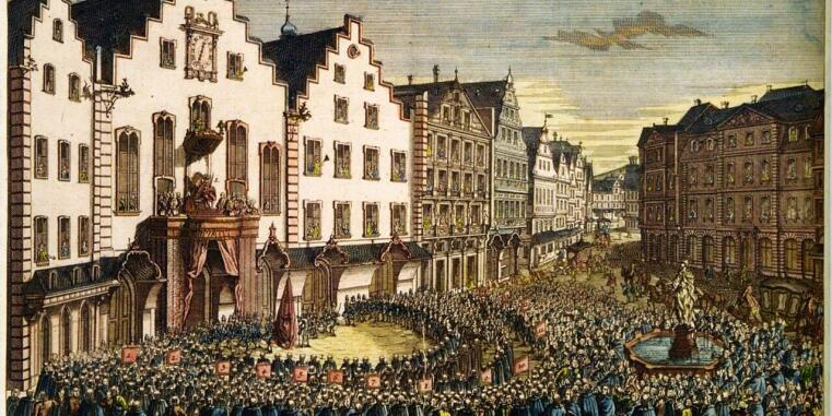 Historische Darstellung einer Stadt mit Gibelhäusern, auf dem Balkon eines der Häuser steht eine Person, auf dem Platz davor stehen dieser Person zugewandt zahlreiche Menschen.