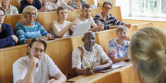 Ältere und jüngere Studierende hören zusammen einer Vorlesung im Hörsaal zu.