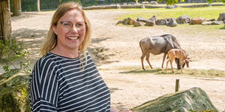 Eine Frau steht vor einem Tiergehege im Zoo.