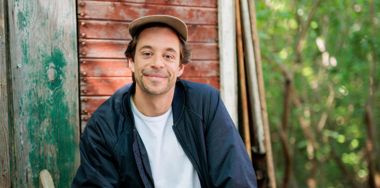 A man is sitting on a little ladder in the woods.