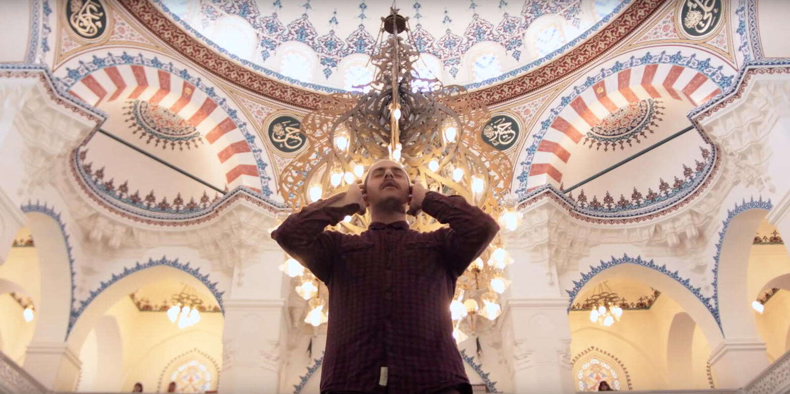 Ein Imam steht unter der Kuppel einer Moschee und ruft aus