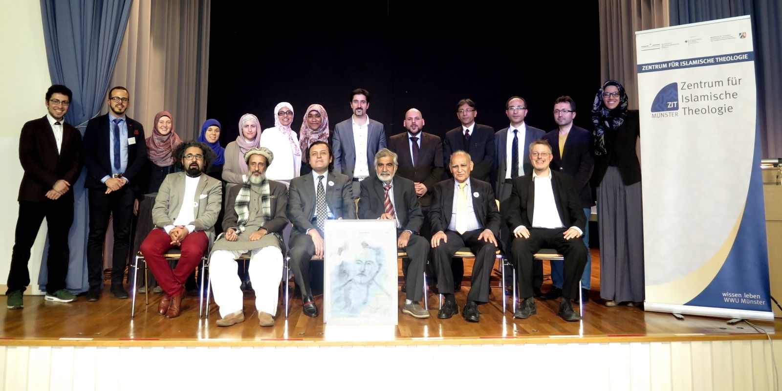Die Referenten und Organisatoren des Symposiums stehend und sitzend, rechts das Roll-up des ZIT, vor der ersten Reihe ein gezeichnetes Porträt von Muhammad Iqbal