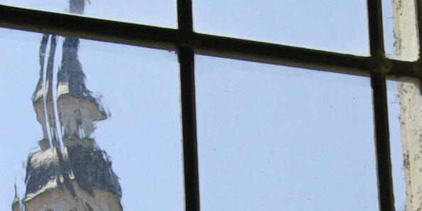 Sprossenfenster, durch welchees das Dach eines alten Gebäudes mit einem kleinen Turm zu sehen ist