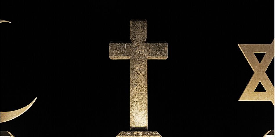 Im Zentrum steht ein Steinkreuz, links sind die Spitzen eines Steinhalbmondes und rechts die zwei linken Zacken eines Davidsterns aus Stein zu sehen vor schwarzem Hintergrund.