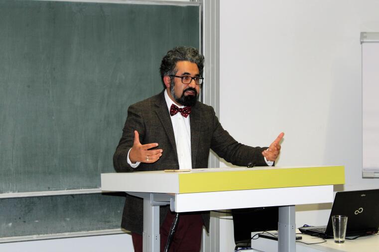 Prof. Karimi steht hinter einem Pult vor einer Tafel