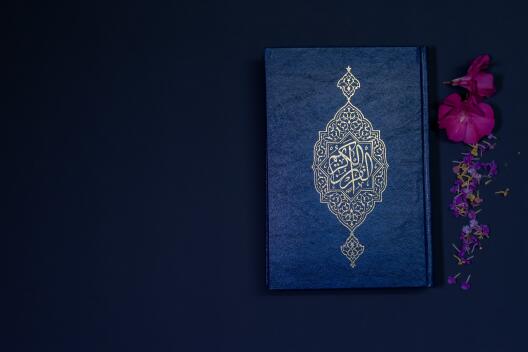 Ein Bild von einem Koran neben einer Blume vor einem dunkelblauen Hintergrund