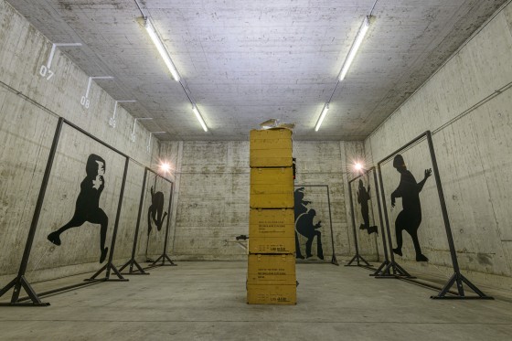 Blick in die aktuelle Ausstellung mit einigen Schattenrissen, die um einen Turm aus ehemaligen Munitionskisten gruppiert sind.