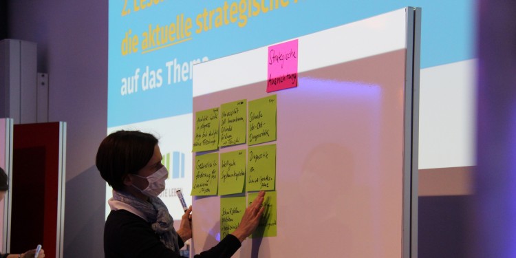 Eine Teilnehmerin befestigt Zettel mit Stichpunkten zur Strategischen Ausrichtung an einer Pinnwand.<address>© Münsterland e.V.</address>