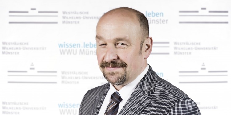 Auf dem Bild ist Prof. Dr. Traugott Roser vor einer Fotowand mit dem Logo der Universität Münster zu sehen.<address>© WWU - Benedikt Weischer</address>