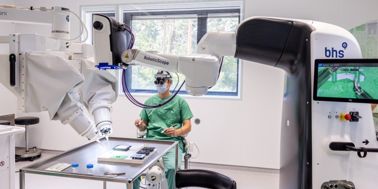 Dr. Maximilian Kückelhaus präsentiert bei einem &quot;Trockentraining&quot; das neue Verfahren. Der Operationsroboter (links) ist mit einem robotischen Mikroskop (rechts) vernetzt.<address>© WWU - Peter Leßmann</address>