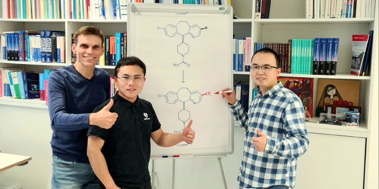 Prof. Armido Studer with Dr. Hui Cao and Dr. Qiang Cheng (from left). The flipchart shows the chemical transformation of loratadine, an important histamine H1-receptor antagonist modified through a trifluoromethyl group.<address>© Münster University – Studer working group</address>