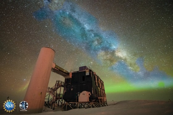 Ein Blick auf das IceCube-Labor mit einem sternenklaren Nachthimmel, der die Milchstraße und grüne Polarlichter zeigt. In Blau darüber gelegt ist das gemessene Neutrino-Signal.<address>© IceCube Collaboration (Yuya Makino)/U.S. National Science Foundation</address>