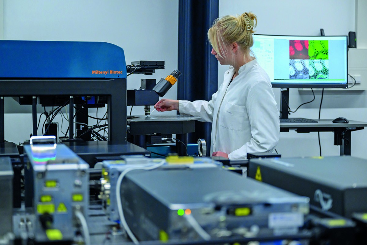 In the foreground are three pulsed infrared lasers which provide excitation light for the microscope. A research associate is preparing a measurement. © University of Münster - Michael C. Möller