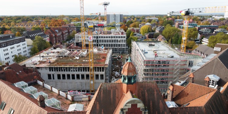 The dimensions of the large-scale Hüffer Campus become clear when seen from the air. The new build of the University of Münster’s future Theologies and Religious Studies Campus can be seen front left, on Robert Koch Straße, and it is linked to the Hüffer Foundation building by a bridge. The roof of the Hüffer Foundation can be seen in the foreground.<address>© Photo: Münster University - Sophie Pieper</address>