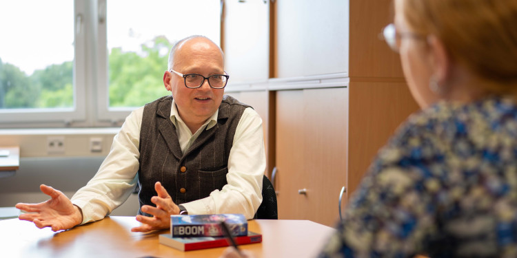 Prof. Dr. Dirk van den Boom brennt für seine Themen. Vor ihm liegen zwei seiner über hundert Science-Fiction-Romane.<address>&copy; Uni MS - Johannes Wulf</address>